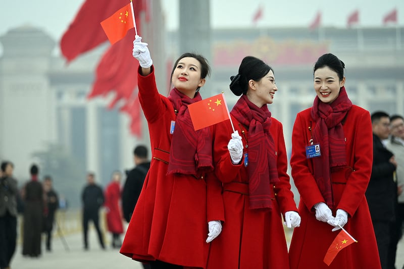 Attendants hold Chinese flags in Tiananmen Square following the closing session of the National People's Congress in Beijing, March 11, 2025.