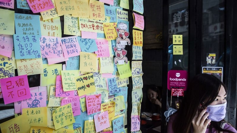A woman stands next to layers of notes on a “Lennon Wall” with messages of support for the pro-democracy protests outside a restaurant in Hong Kong, July 3, 2020,