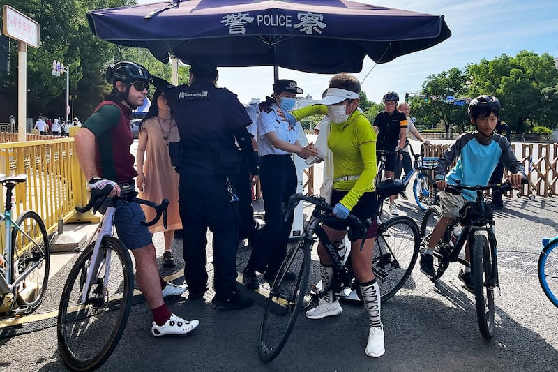 2023年6月4日,一名骑车的外国人(左一)在北京东长安街的安检点等待身份检查。(美联社)